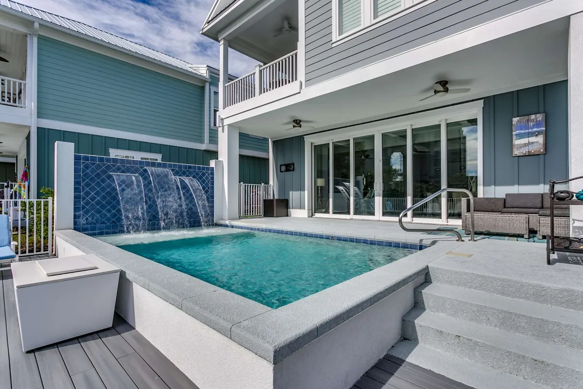 An inviting outdoor scene featuring a swimming pool with a waterfall, surrounded by comfortable seating. The area is set for outdoor dining and relaxation, evoking a sense of cozy gatherings and sunset swims.