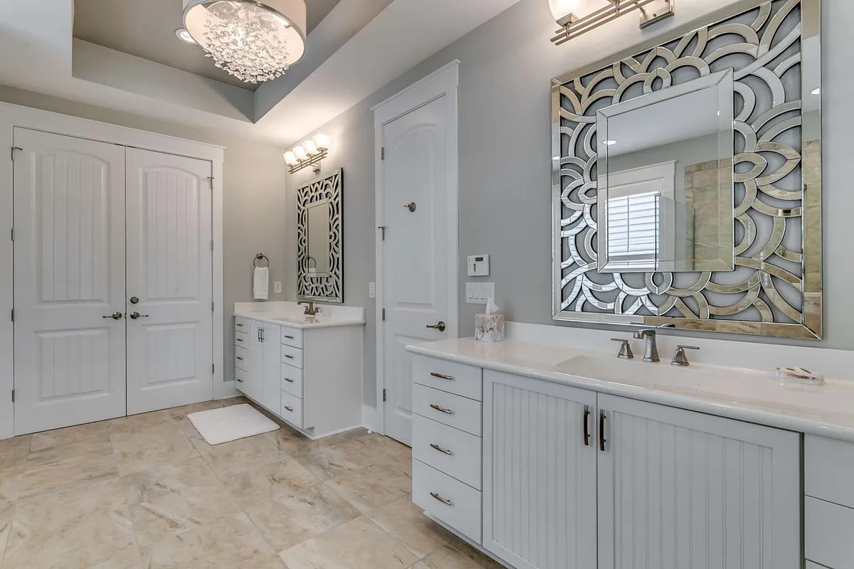 A luxurious en-suite bathroom featuring dual sinks, elegant decorative mirrors, and chandelier lighting. Sliding doors suggest privacy, while the spacious layout hints at a spa-like experience for unwinding after a busy day.