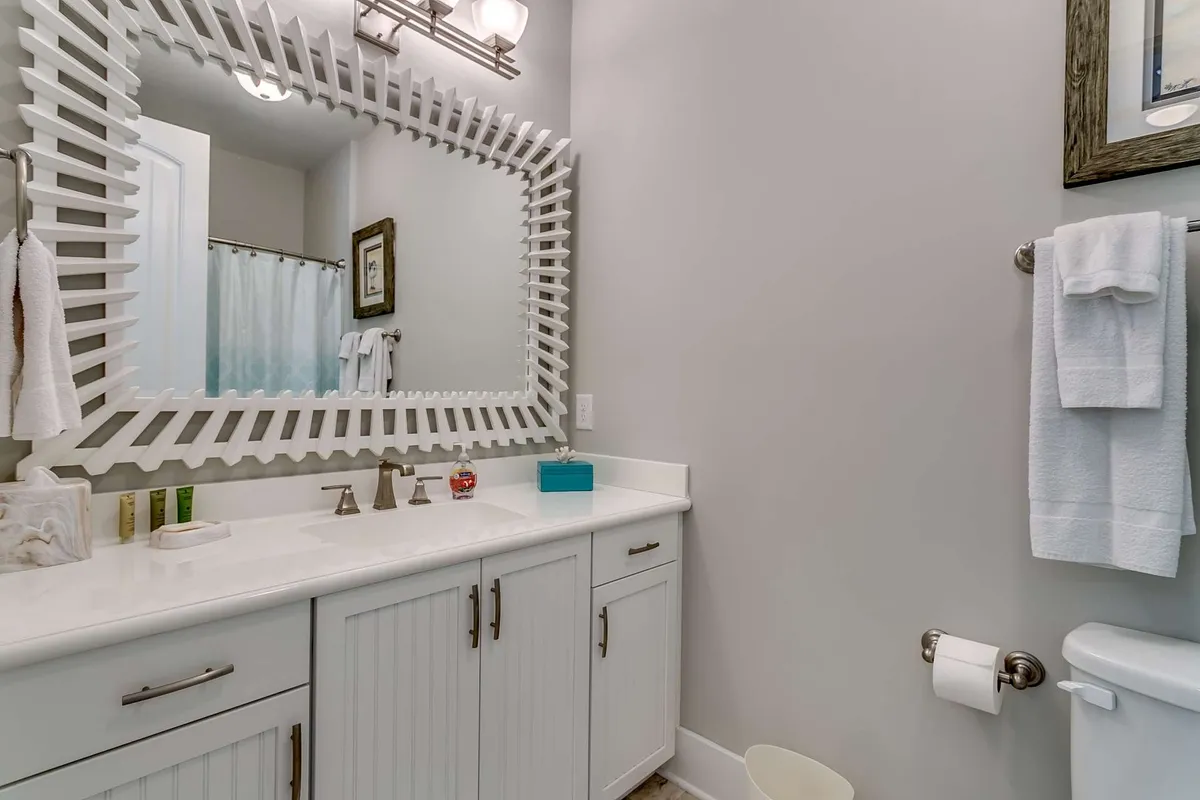 A tranquil bathroom interior with a large decorative mirror, crisp white cabinetry, and a sleek sink area. The space glows with natural light, evoking a sense of freshness and refined comfort—perfect for self-care and wellness routines.