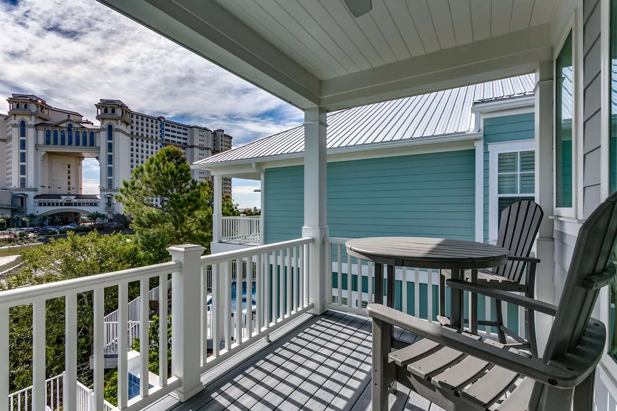 A spacious balcony furnished for comfort, looking out over a resort area with distant views of green trees and blue sky. The balcony suggests a peaceful vantage point for enjoying ocean breezes, sunrises, or sunsets with friends or family.