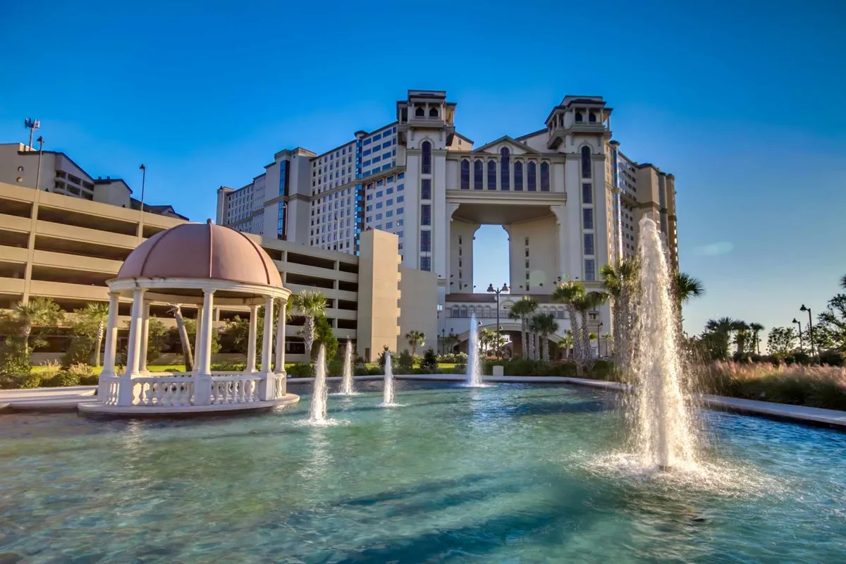 An elegant exterior scene featuring a sparkling water fountain, a charming gazebo, and a grand building archway, all set within lush landscaping. The scene exudes a sense of luxury and relaxation, ideal for groups gathering or unwinding.