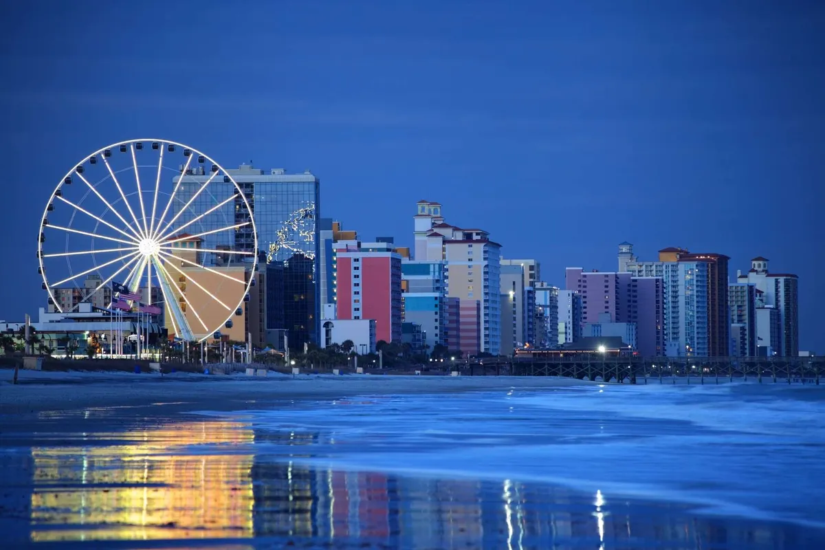 A colorful exterior scene with a Ferris wheel, vibrant buildings, and reflective water, suggesting a lively beachfront amusement area. The atmosphere is festive and energetic, hinting at a wealth of entertainment options.