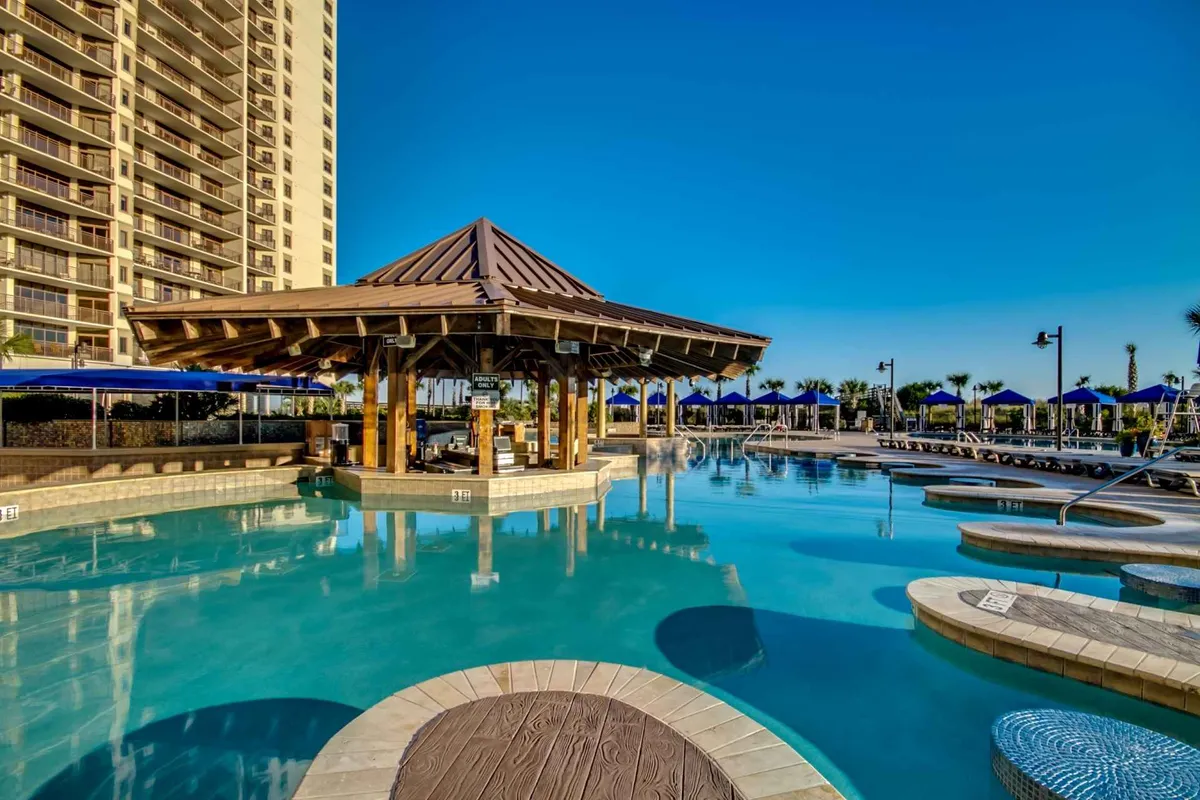 A serene pool area featuring a thatched-roof gazebo, rows of lounge chairs, and lush palm trees. The setting is peaceful, offering a spot for morning yoga, poolside drinks, or quiet relaxation, with a clear view of the resort's inviting outdoor spaces.