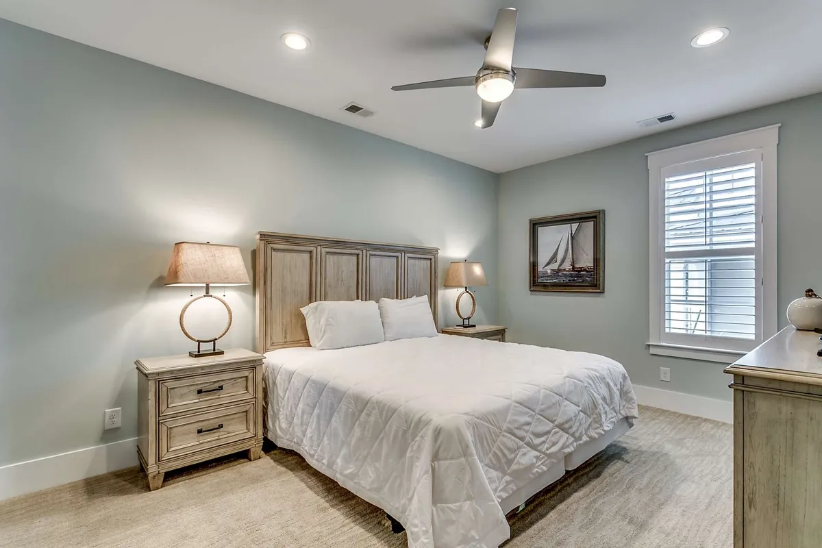 A tranquil bedroom with a cozy bed flanked by nightstands, soft lamps, and framed artwork. A window allows gentle daylight to filter in, creating an inviting atmosphere perfect for relaxation or quiet reading.